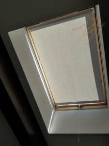 Открытые рулонные шторы на мансардном окне в салоне с тканью Luminis T 05 Grey