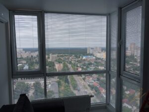 Белые горизонтальные жалюзи на струне, установленные на панорамное окно с отличным видом.